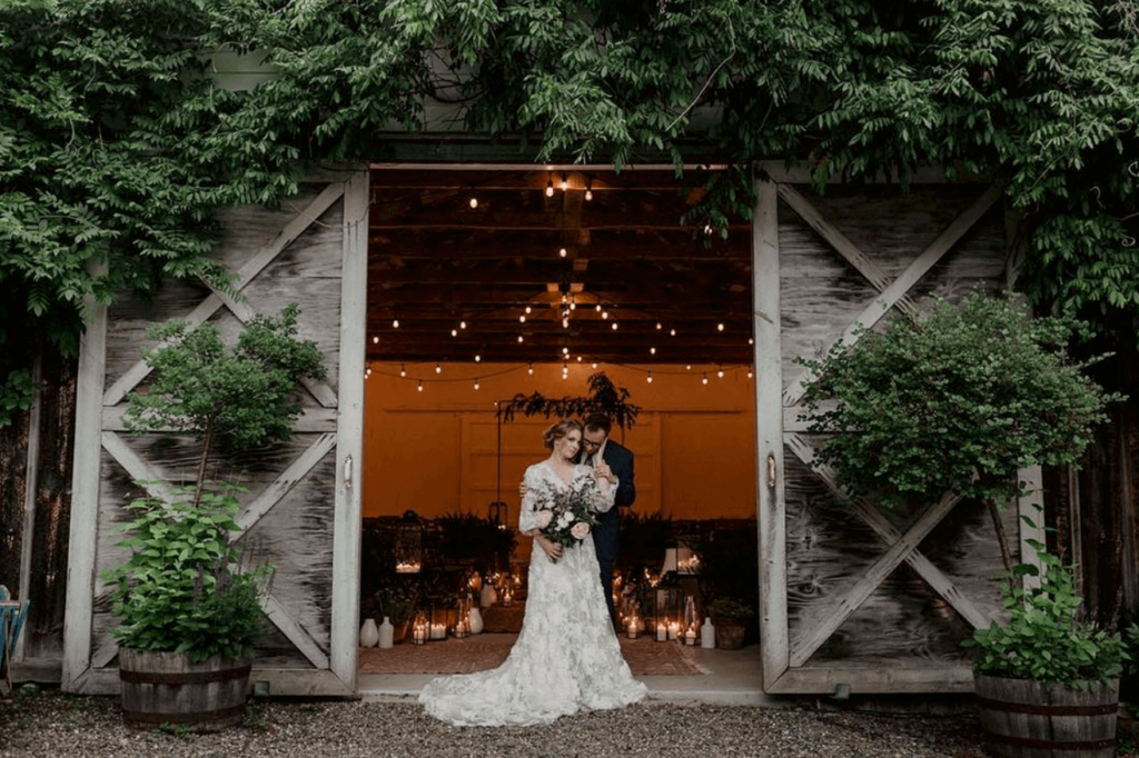 Newlywed couple poses in front of a rustic barn. 